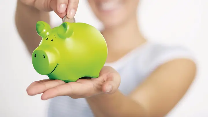 Man sieht eine Frau, die Geld in ein grünes Sparschwein wirft.