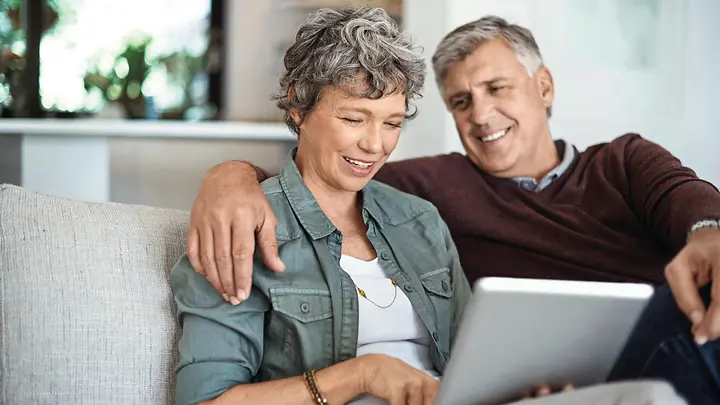 Ein Mann und eine Frau sitzen auf einem Sofa und schauen auf ein Tablet.