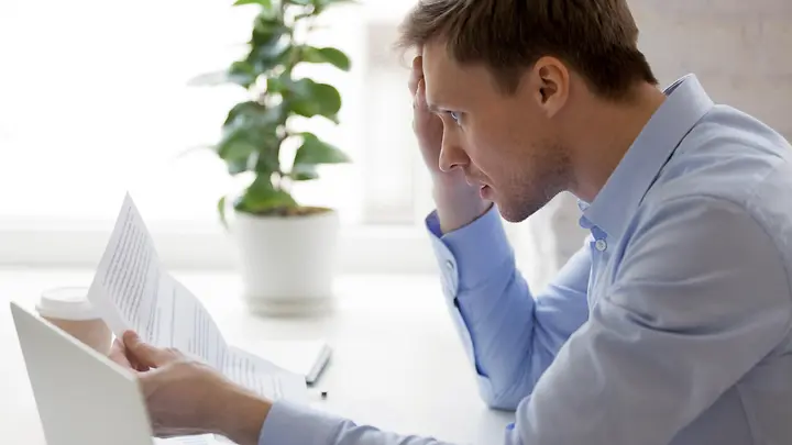 Man sieht einen Mann, der sich die Haare rauft und auf ein Dokument schaut.