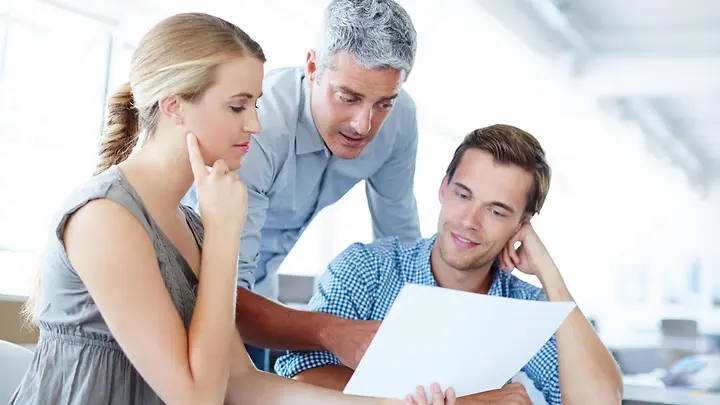 Man sieht eine Frau und einen Mann, die von einem Mann beraten werden.