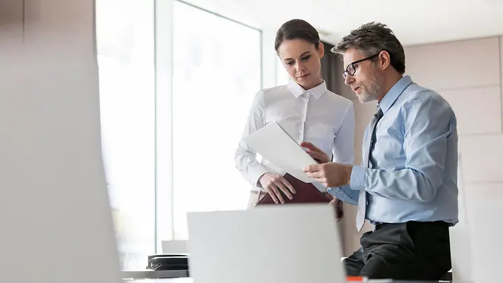 Man sieht eine Frau und einen Mann, die auf einen Dokument schauen.