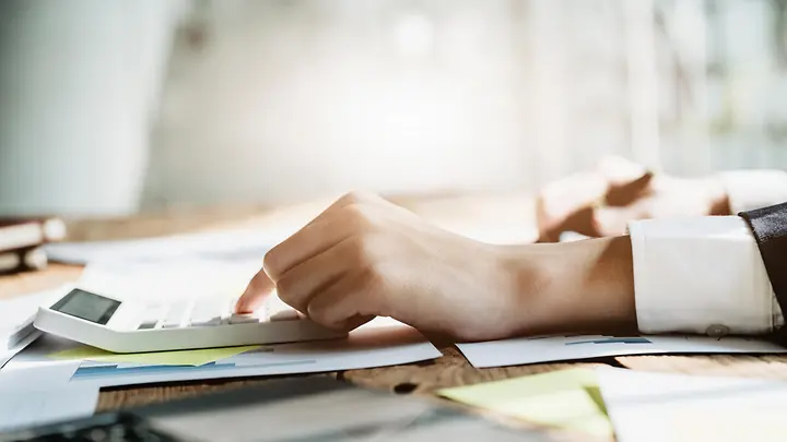 Man sieht eine Hand, die einen Stift hält und etwas in den Taschenrechner tippt.