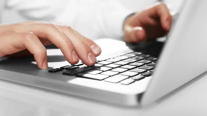 Eine Hand tippt etwas in einen Laptop.