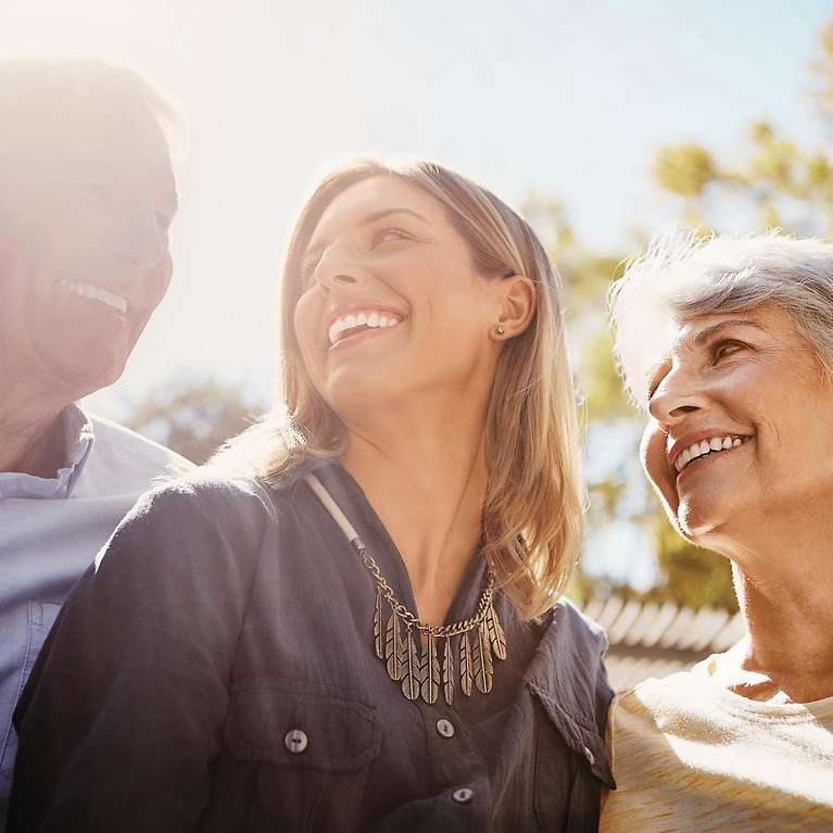 Eine junge Frau lächelt eine ältere Frau und einen älteren Mann an.