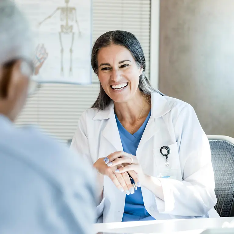 Man sieht eine Zahnärztin, die lächelt und sich mit einem Patienten unterhält.