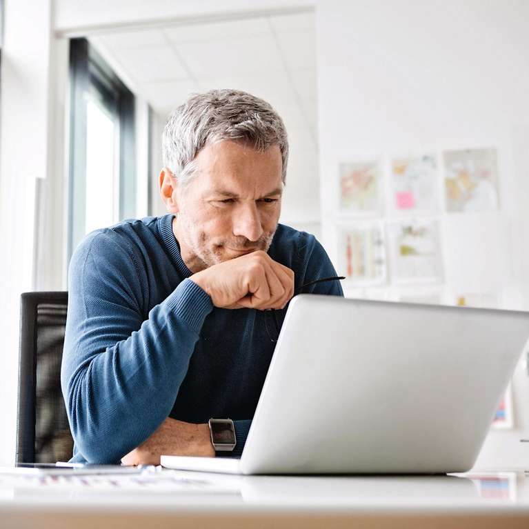 Ein Mann, der nachdenklich auf seinen Laptop schaut und überlegt.