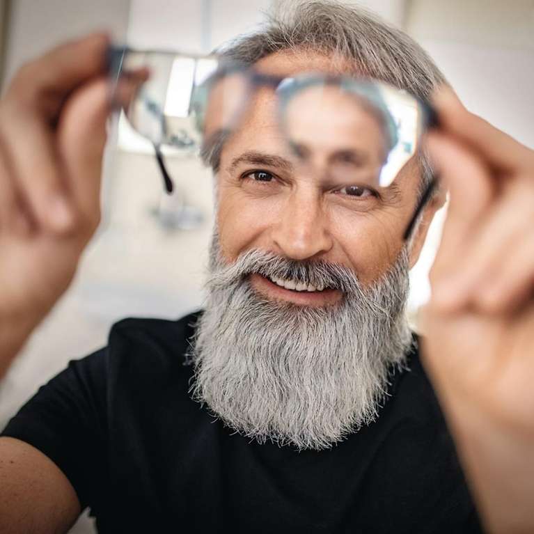 Ein Mann hält lächelnd eine Brille vor sein Gesicht.