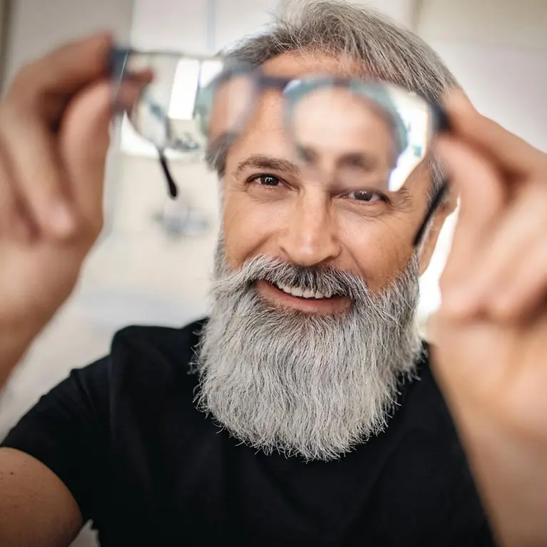 Ein Mann hält lächelnd eine Brille vor sein Gesicht.