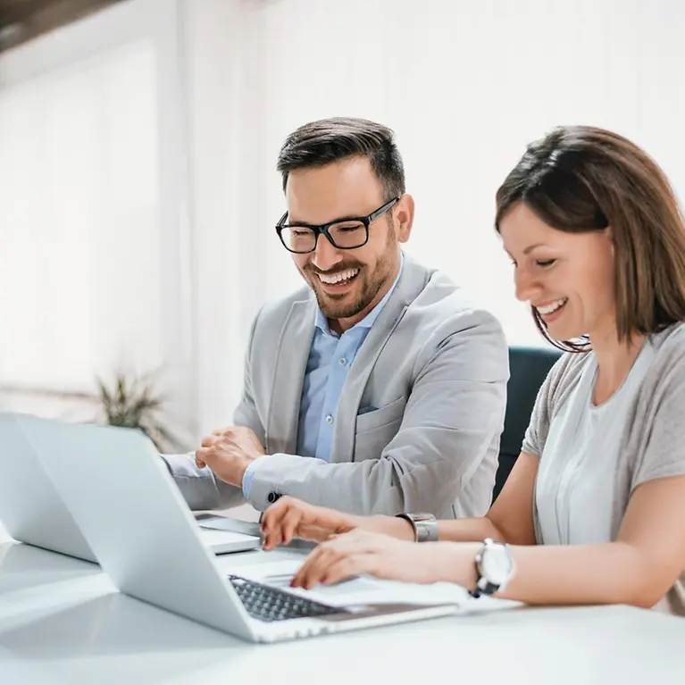 Ein Mann und eine Frau schauen auf einen Laptop und lächeln.
